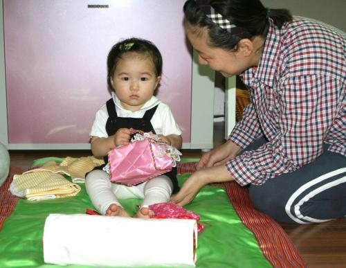 동생이 선물받은 비단 이부자리가 좋은 듯 이불 위에 앉아 이것저것 만져보는 큰딸 '민'이. 